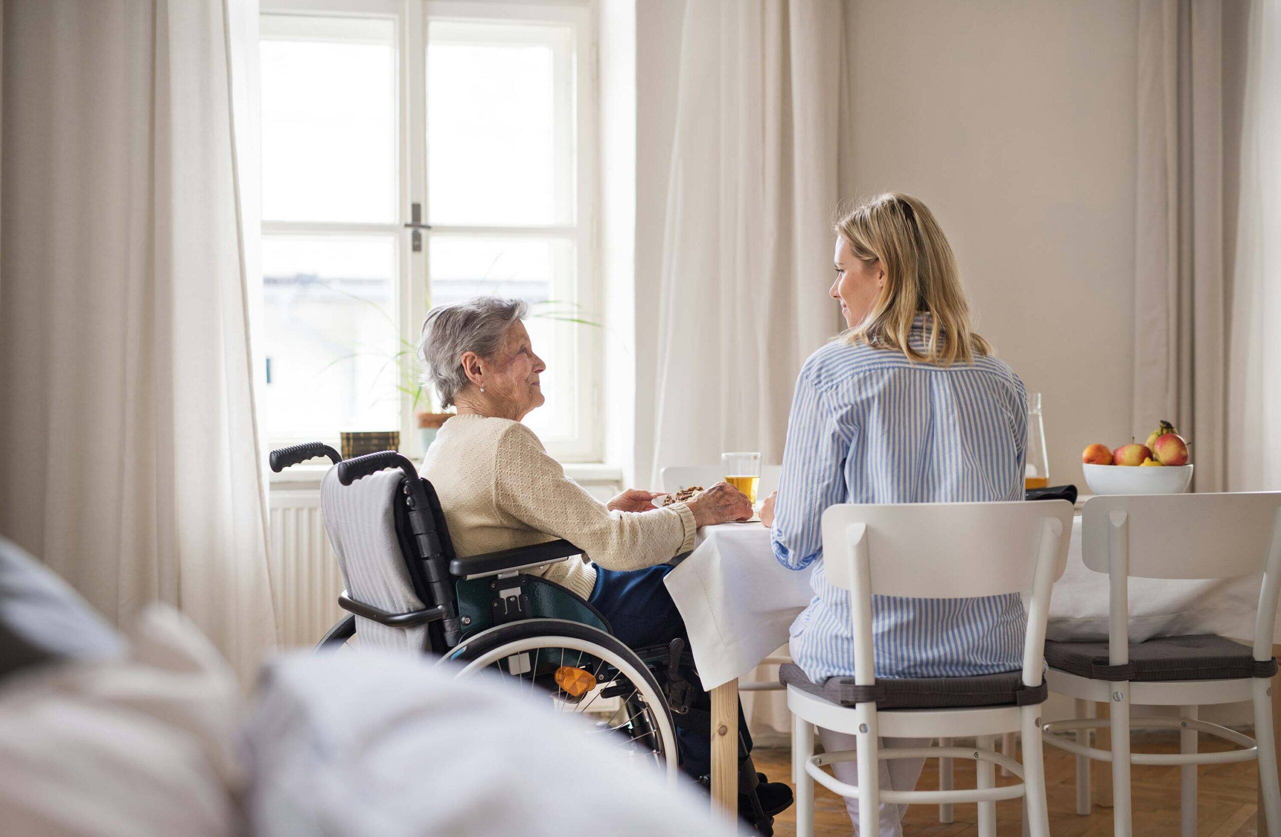 Betreuungskraft und ältere Frau sitzen gemeinsam am Esstisch